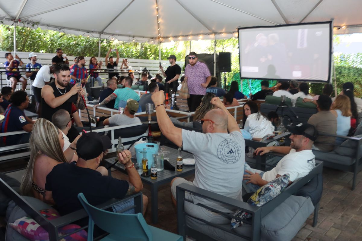 Soccer fans celebrating a goal on the projection big screen while sharing hookah and beers on the covered Miami Vice patio at Grails Miami, Miami's Thursday-night Europa League bar