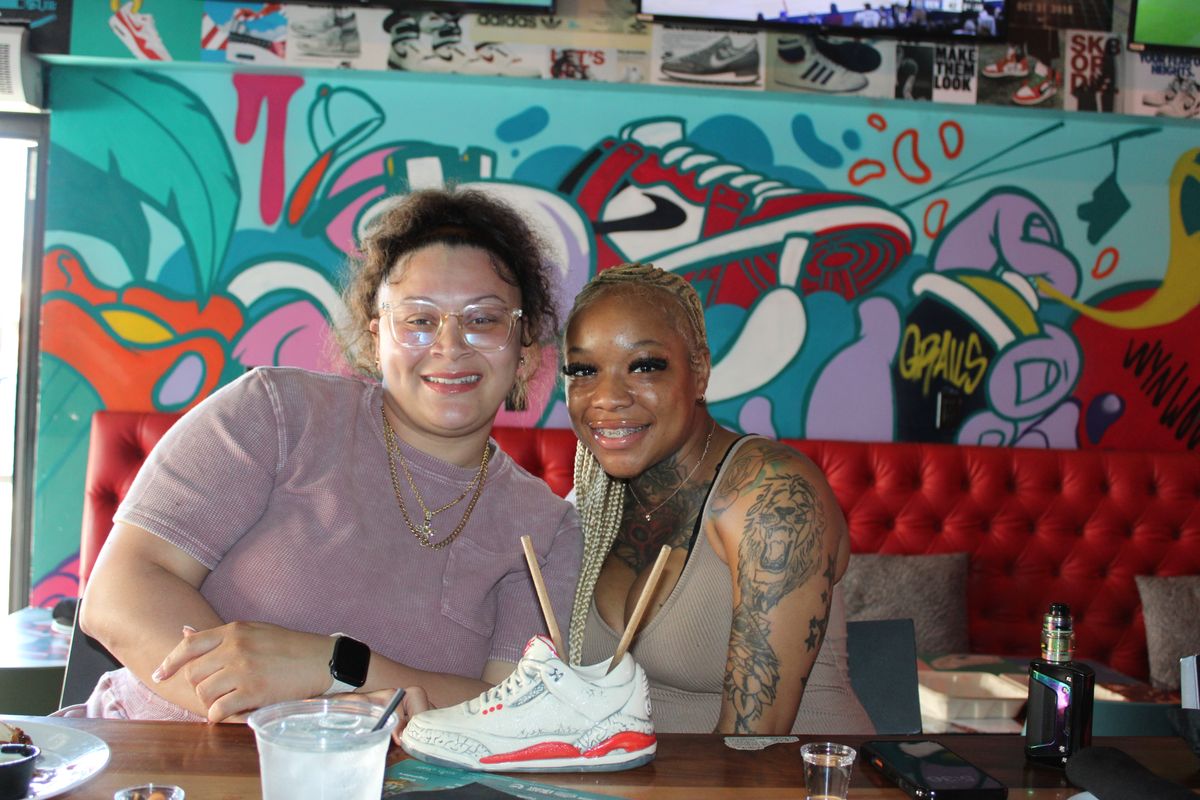 Two friends with the Grails sneaker cocktail in a red booth under the Wynwood mural, the game-day ritual at Miami's FSU watch party bar