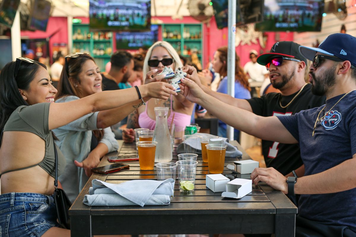 Group of friends reaching across the table for a toast with drinks during a game night at Grails Miami