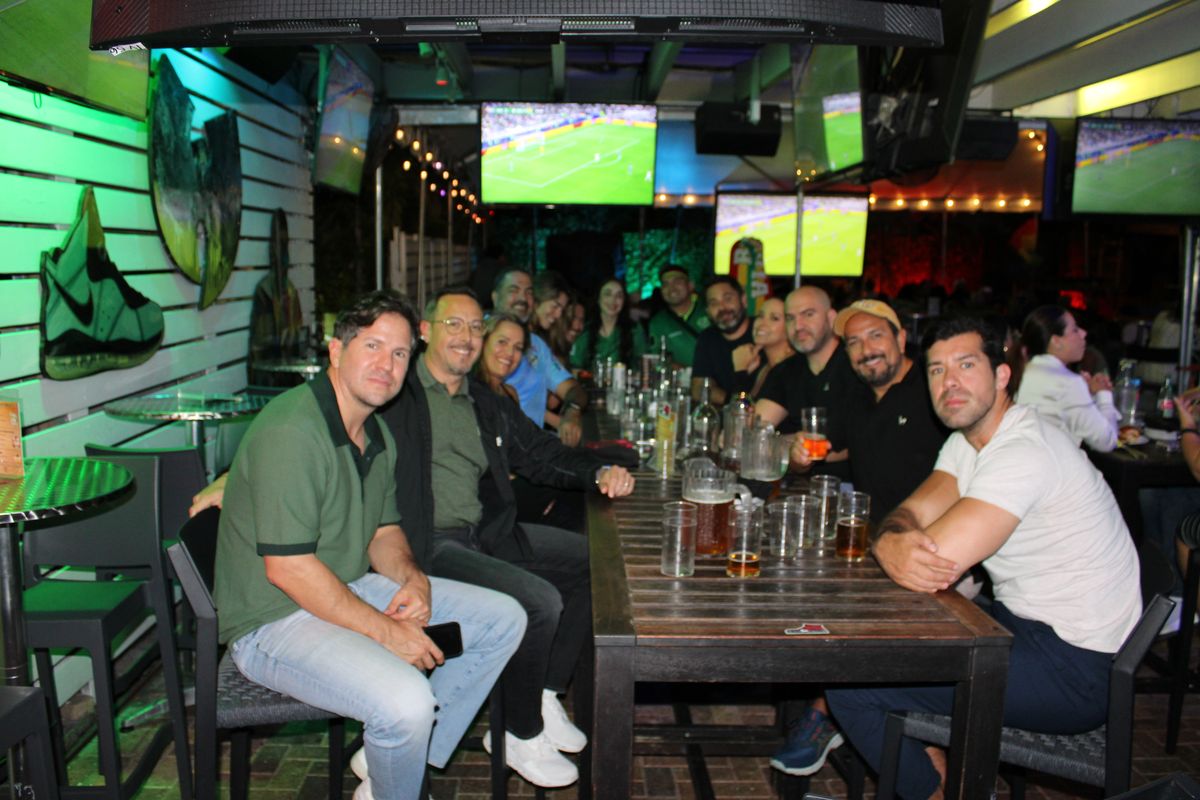 Large group of friends posing together at a long indoor table during an Italian football watch party at Grails Wynwood Miami