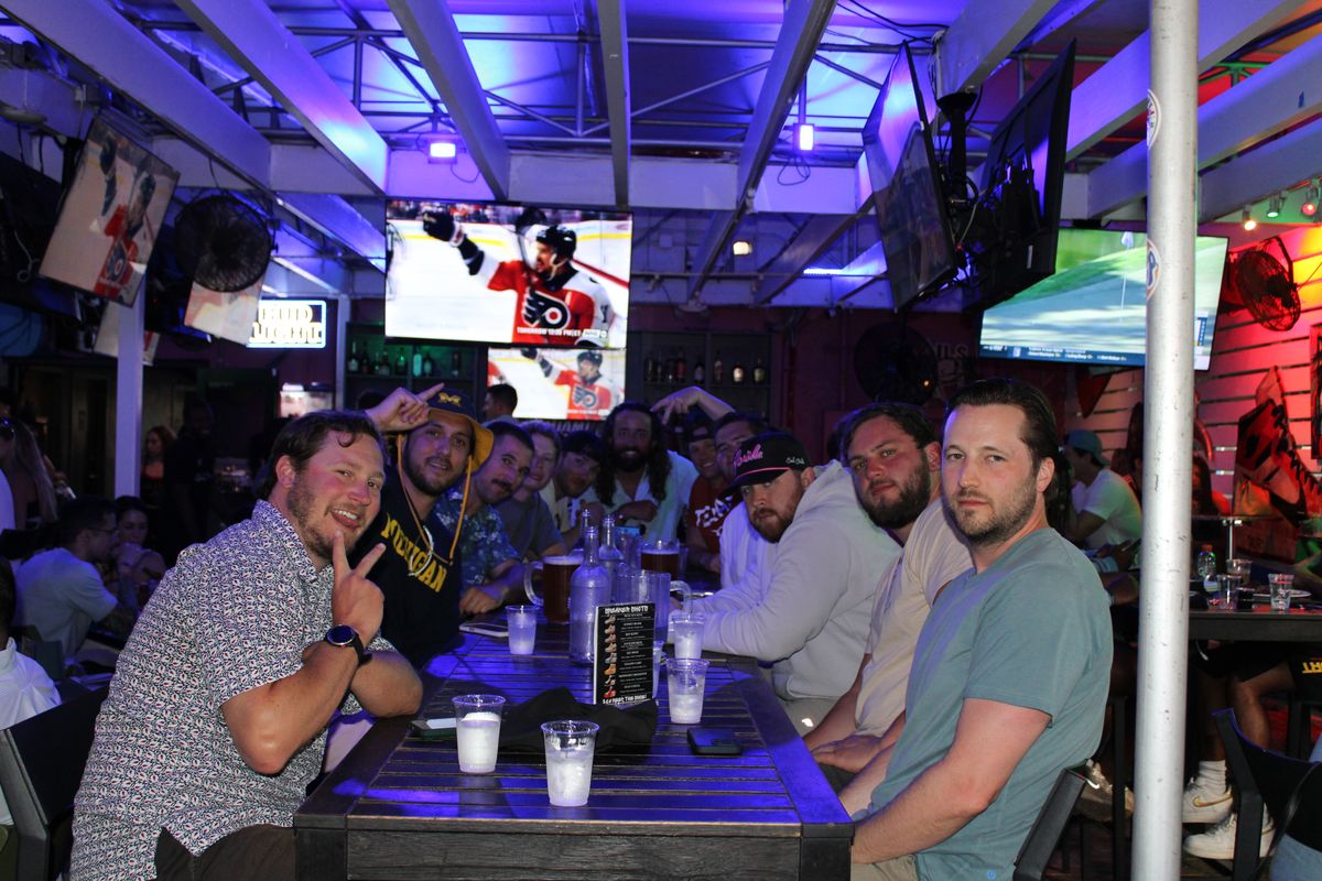 Large group of friends gathered around a long table with beer pitchers at Grails Wynwood while an NHL Stanley Cup Playoff game plays overhead