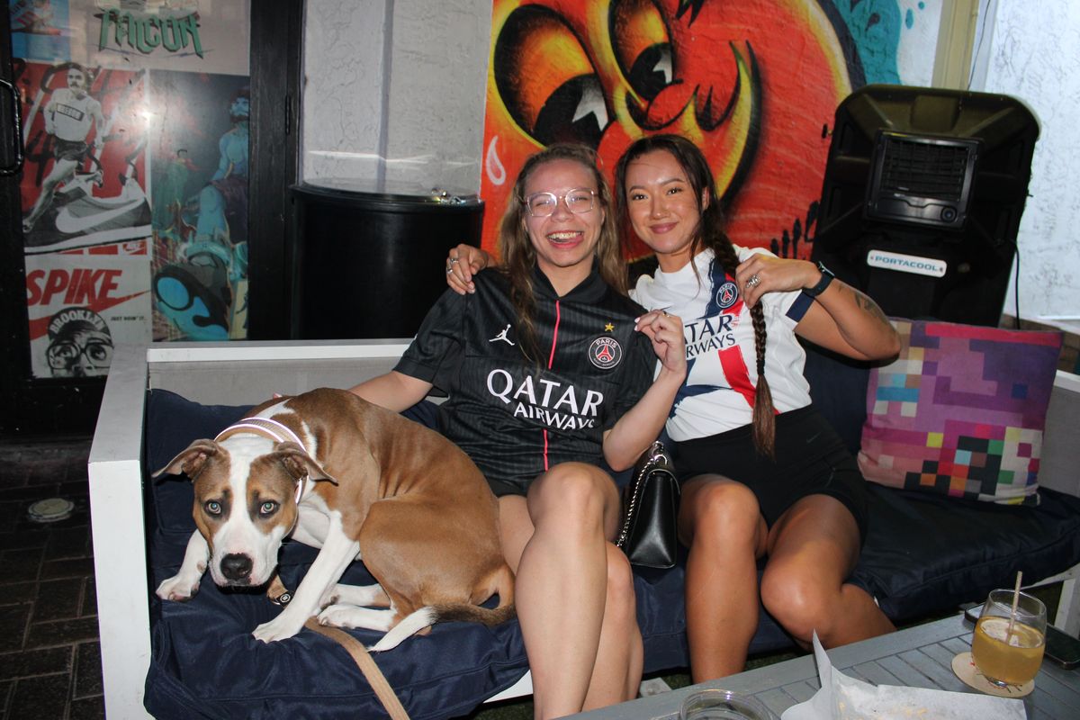 Two Paris Saint-Germain fans in PSG jerseys posing with a pit bull during a European soccer watch party at Grails Wynwood, Miami's UEFA Europa League pub