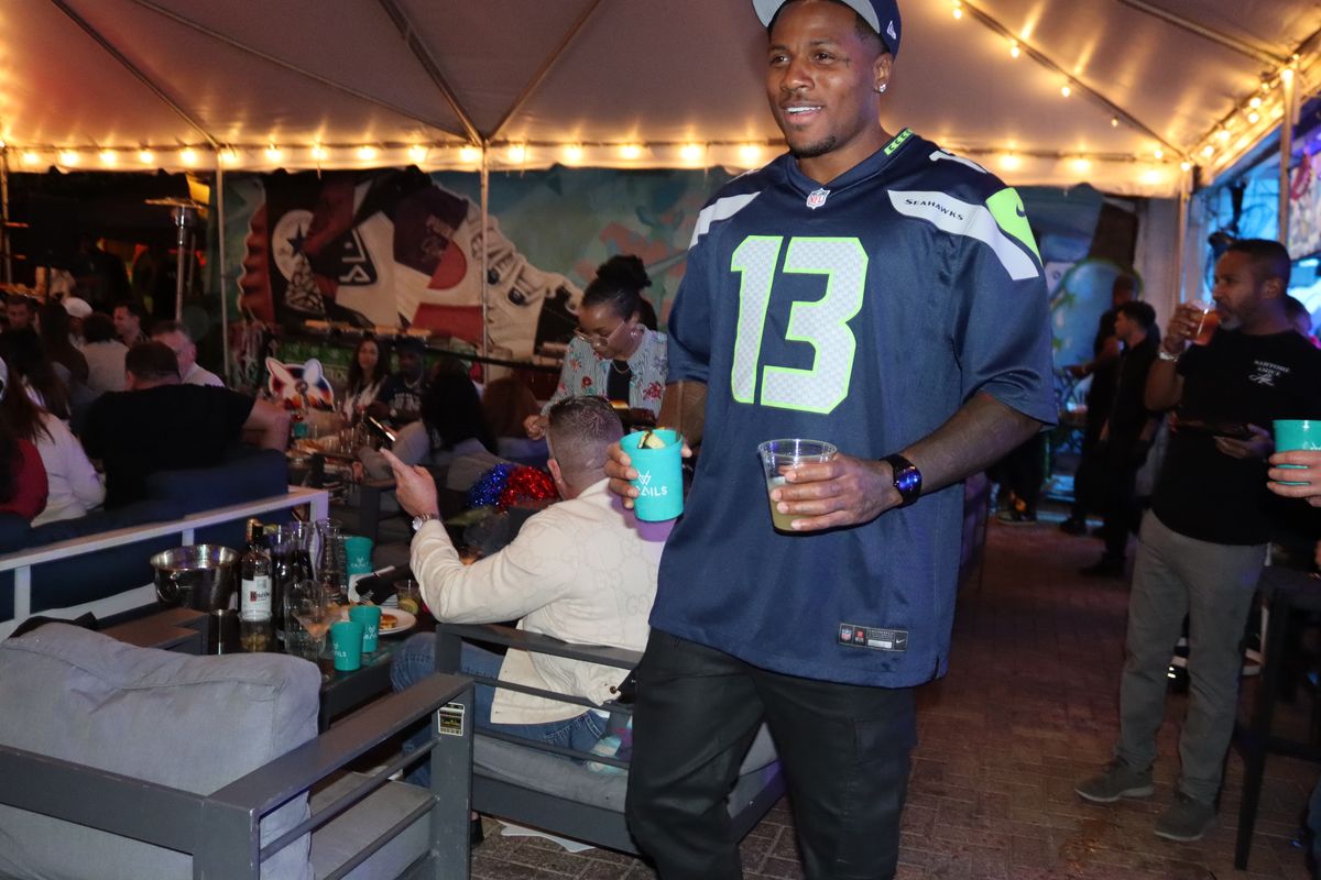 Fan in a Seahawks number 13 jersey holding a cocktail under the string lights of the tented patio at Grails Miami