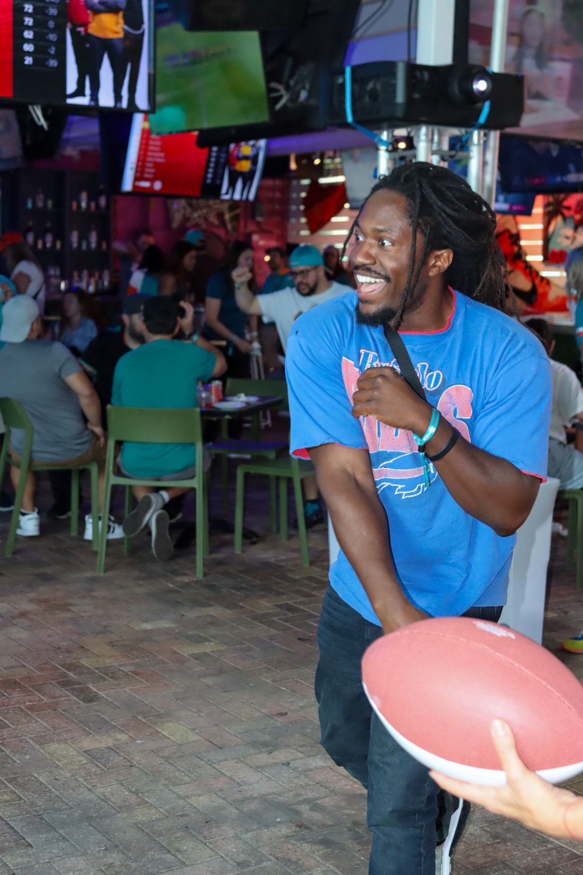 Buffalo Bills fan in a blue Bills tee laughing mid-catch during a football toss at a Grails Miami NFL watch party