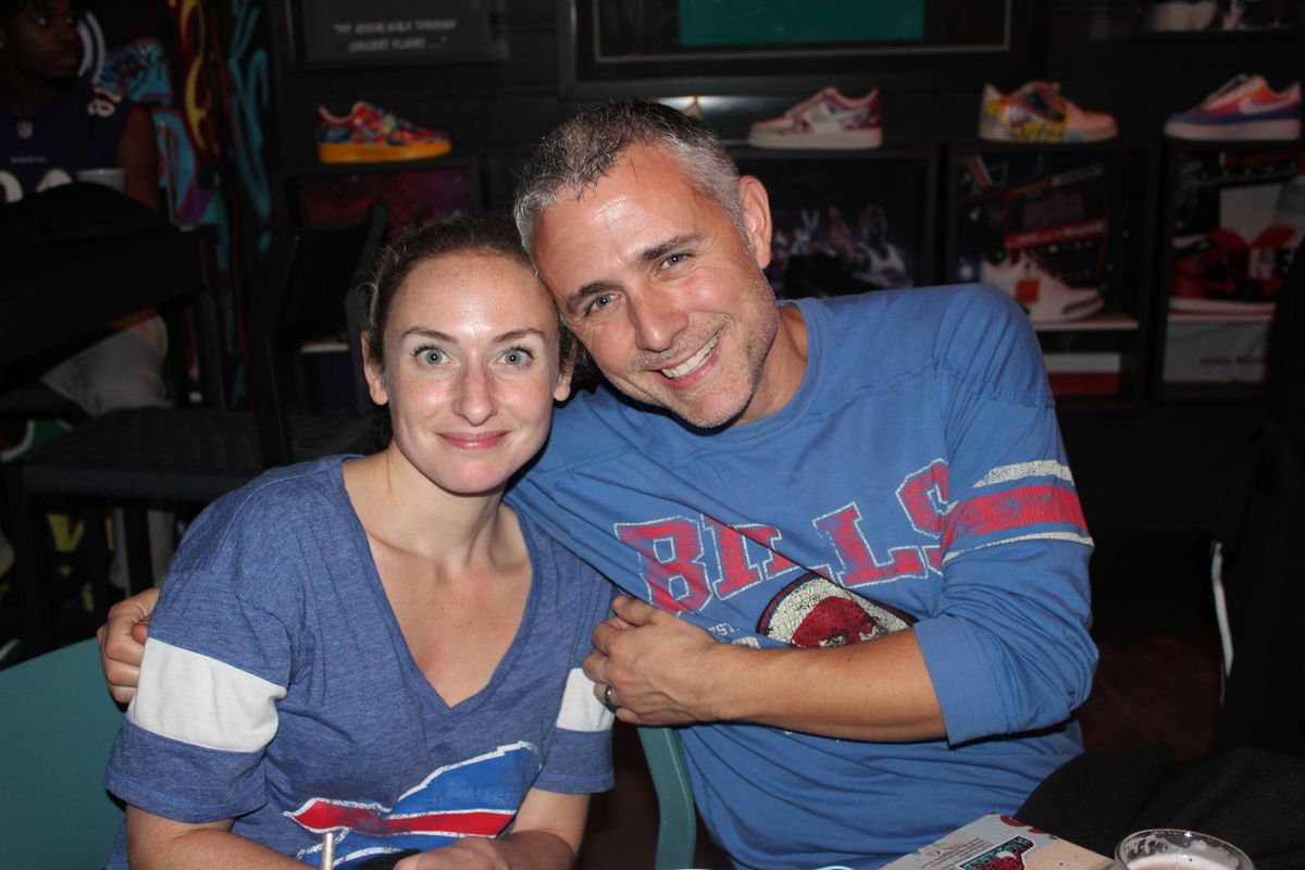 Couple in Buffalo Bills shirts in front of the custom sneaker wall in the indoor sneaker lounge at Grails Miami