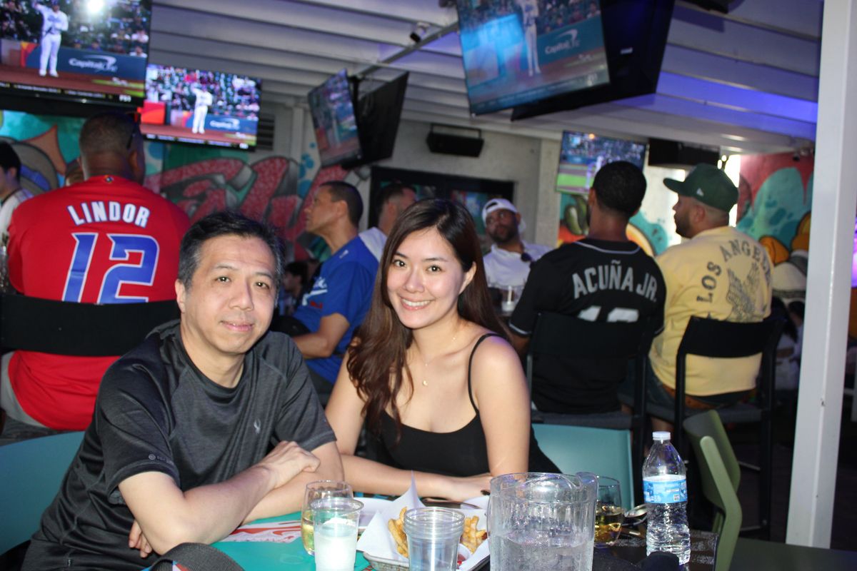 Couple at a Grails Wynwood table during a Miami Marlins watch party with Lindor and Acuña Jr. jerseys visible nearby