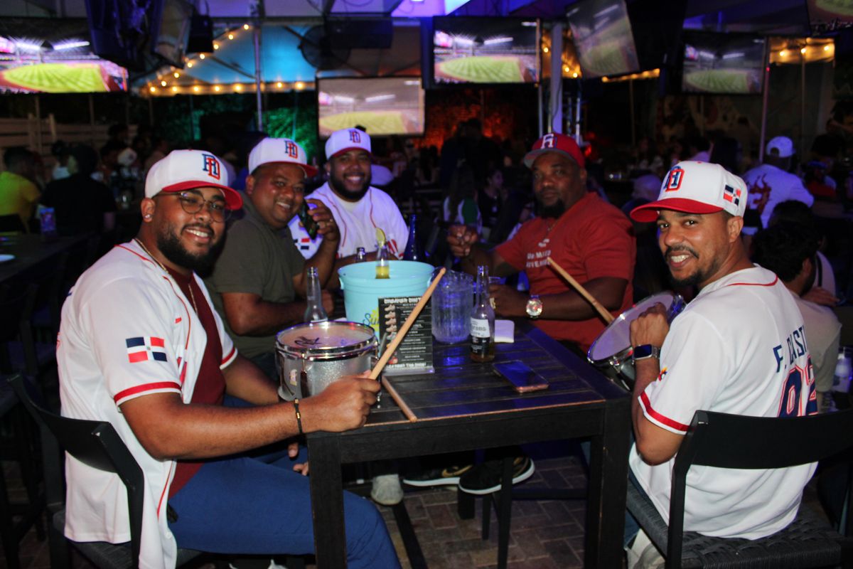 Group of Dominican Republic baseball fans in matching jerseys with snare drums and Coronas around a Grails Wynwood table during a Miami Marlins watch party