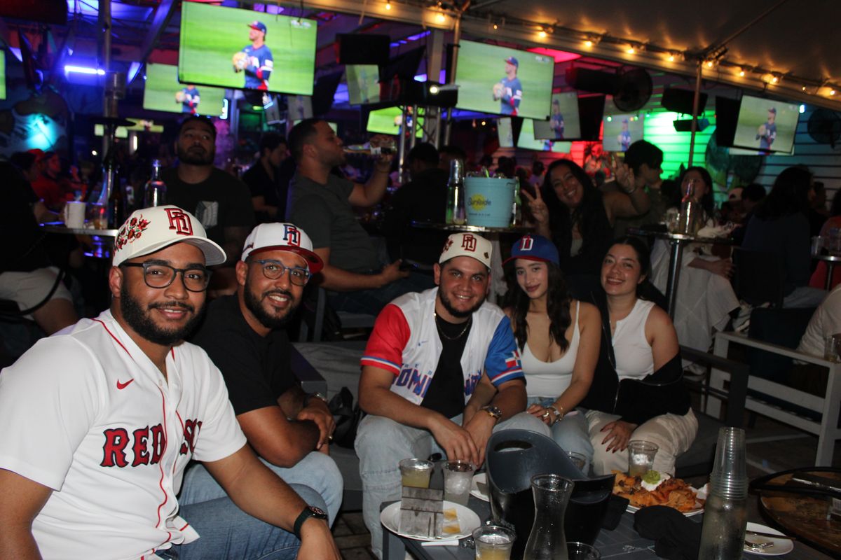 Group of Dominican Republic baseball fans cheering at a Grails Wynwood table during a World Series watch party