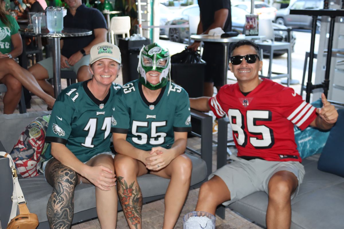 Two Philadelphia Eagles fans in number 11 and number 55 jerseys sitting with a rival fan on the patio couches at Grails Miami