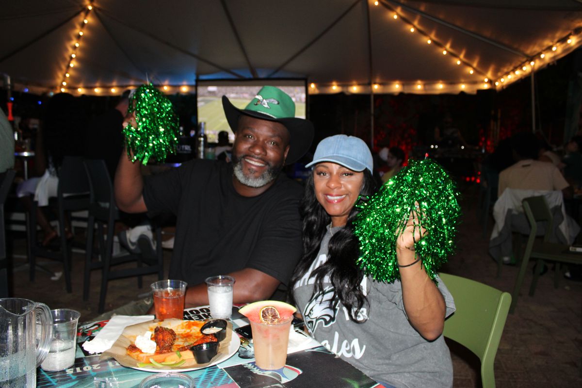 Philadelphia Eagles fan couple in team gear waving green pom-poms over wings and cocktails at the Eagles bar in Wynwood, Miami