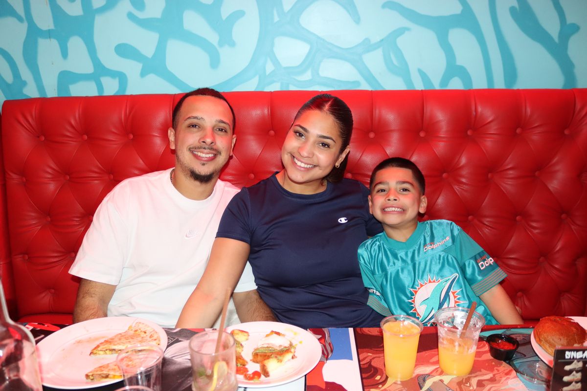 Family of three at a red booth at Grails Wynwood with the son in a Miami Dolphins #1 jersey