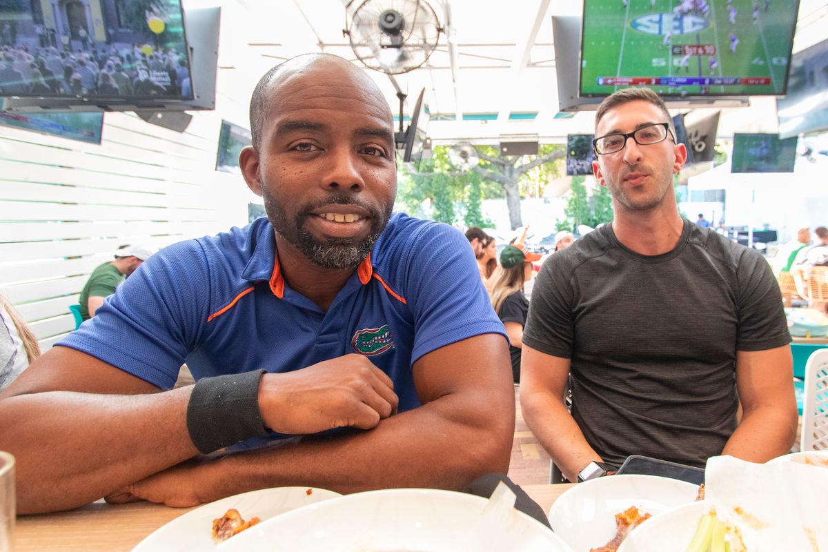 Florida Gators fan in a blue Gators polo at a covered patio table at Grails Miami with an SEC game on the TVs overhead