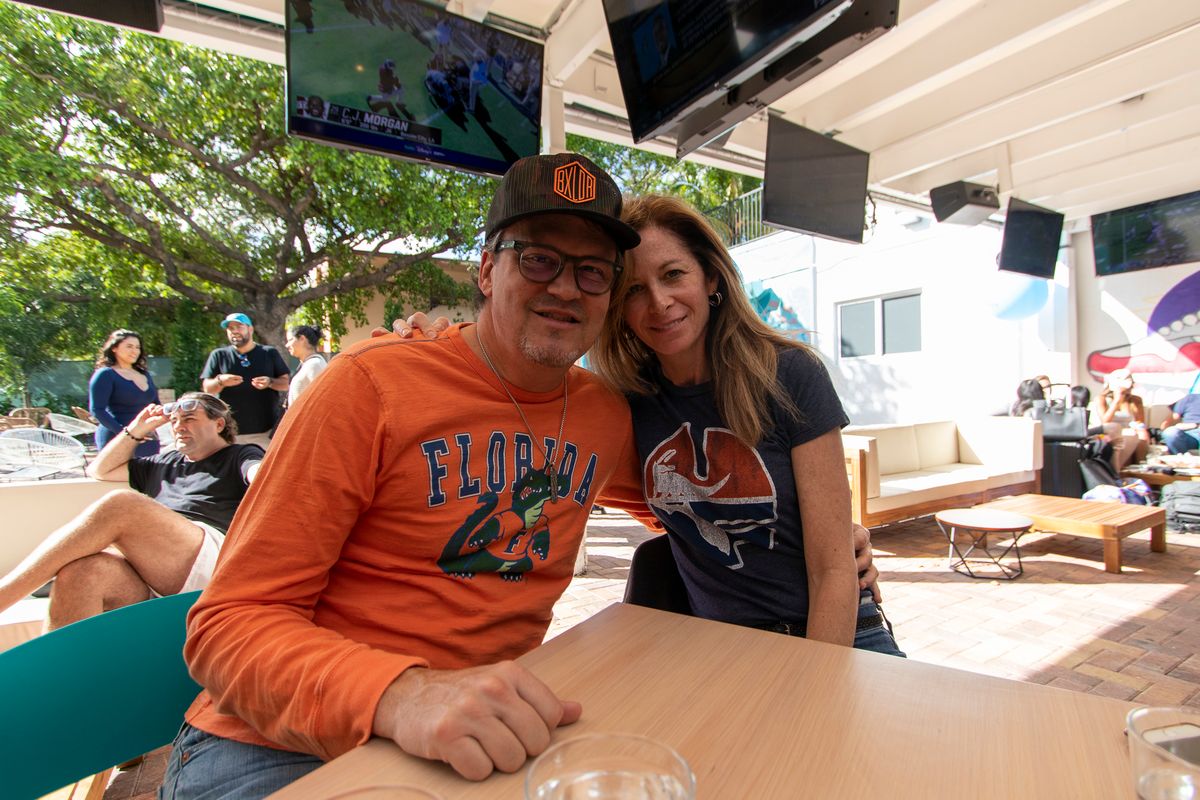 Couple on the Grails Miami patio, one in an orange Florida Gators shirt, with the game on the TVs behind them