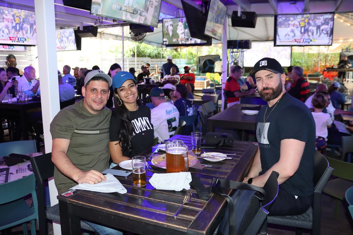 Three friends at a covered patio table at Grails Miami with college football on the TVs above them on a Florida State Seminoles Saturday