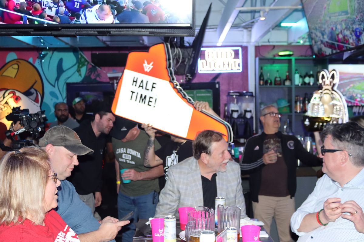 Oversized orange sneaker halftime sign raised over a crowded table of football fans at Grails Miami, Miami's Thursday Night Football watch party bar