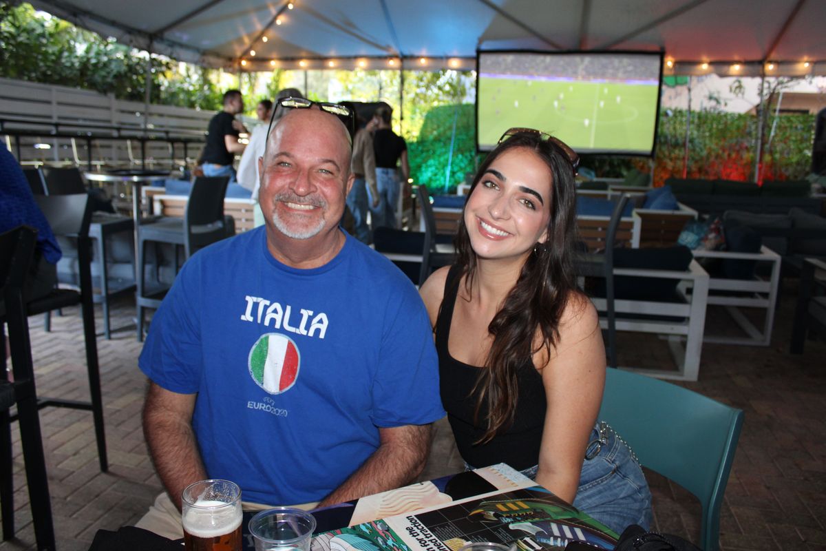 Smiling Italian football fan in an Italia shirt and a friend posing at a Grails Wynwood patio table during a Serie A watch party