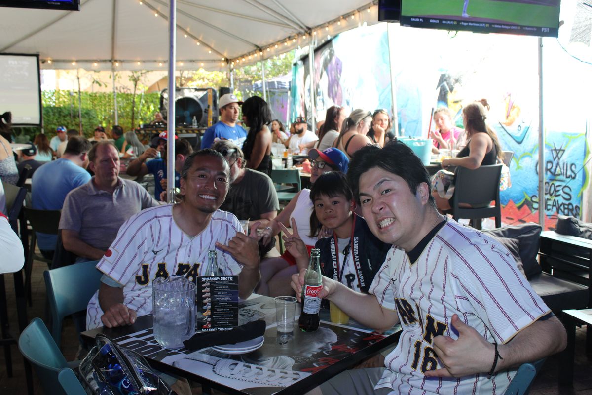 Two friends in Japan Samurai baseball jerseys at a Grails Wynwood patio table during a World Series watch party