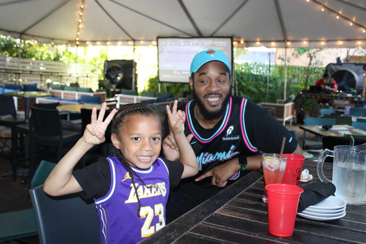 Father and child in Lakers and Miami Heat jerseys watching the NBA on the Grails Wynwood patio