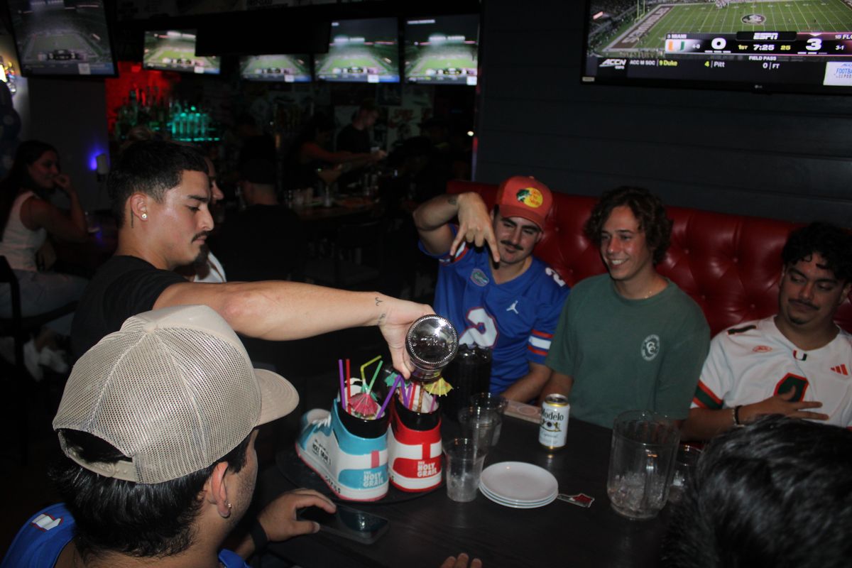 Server pouring drinks into sneaker cocktails for a booth of Florida Gators fans at Grails Miami, Miami's Gators sports bar
