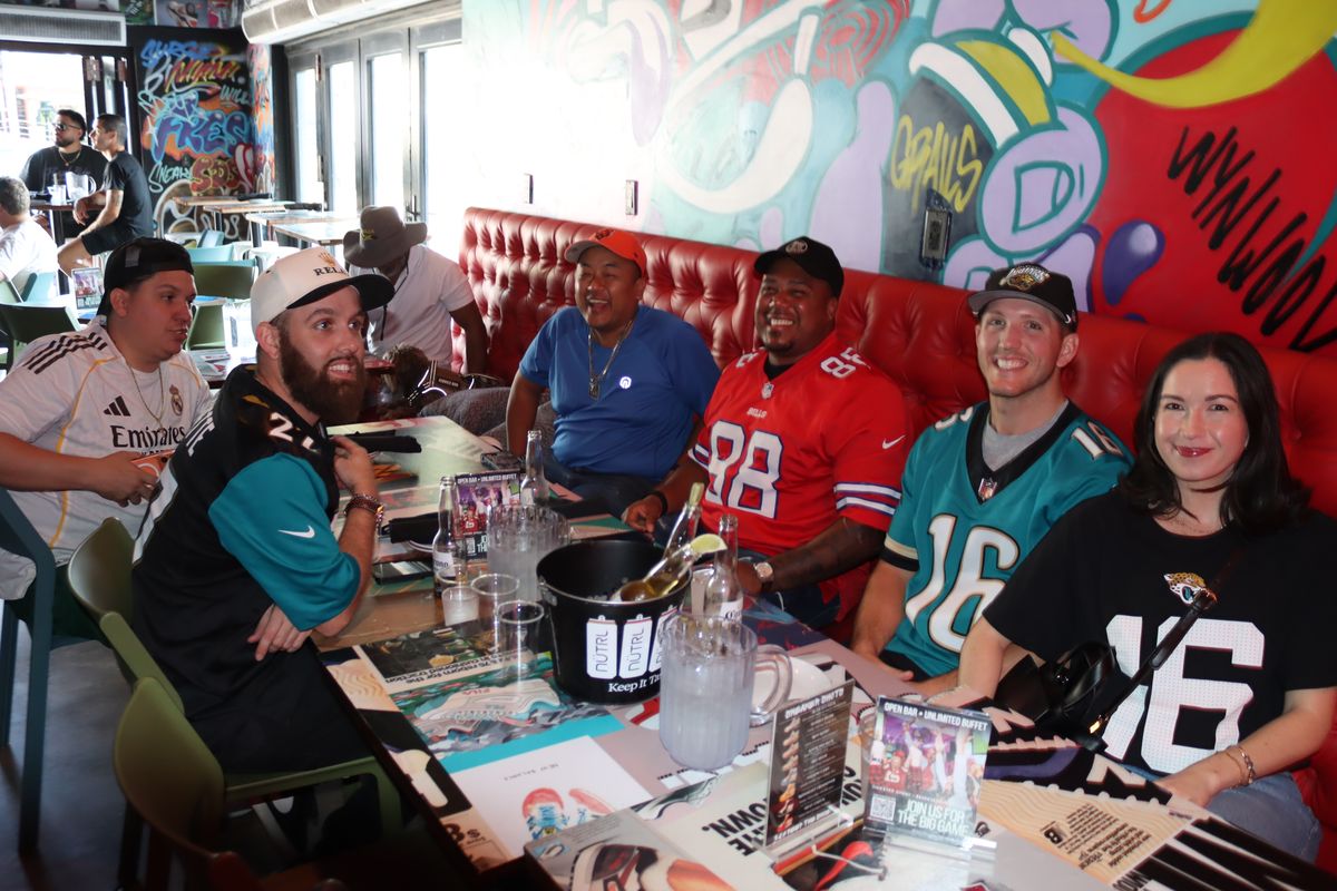 Group of fans in Jaguars and Bills jerseys around a red booth table at a Monday Night Football watch party in Miami