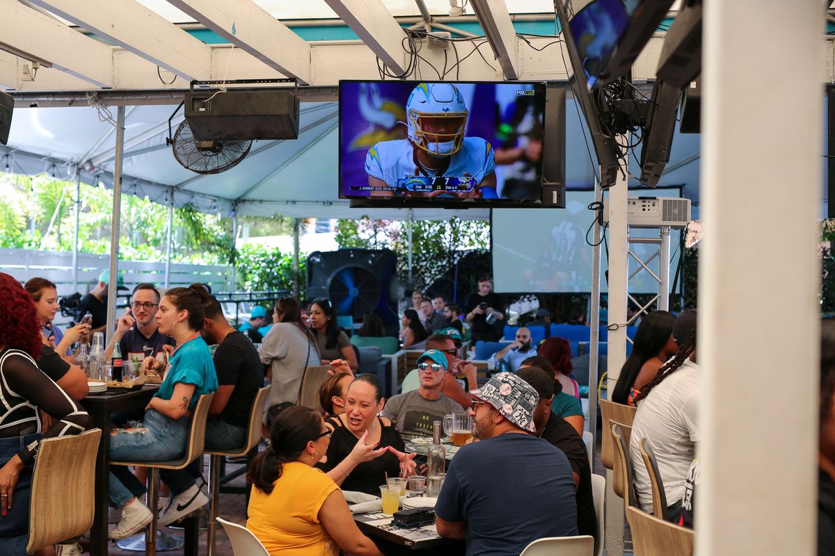 Full covered patio of football fans watching an NFL game on the overhead TVs at Grails Miami in Wynwood, minutes from Edgewater