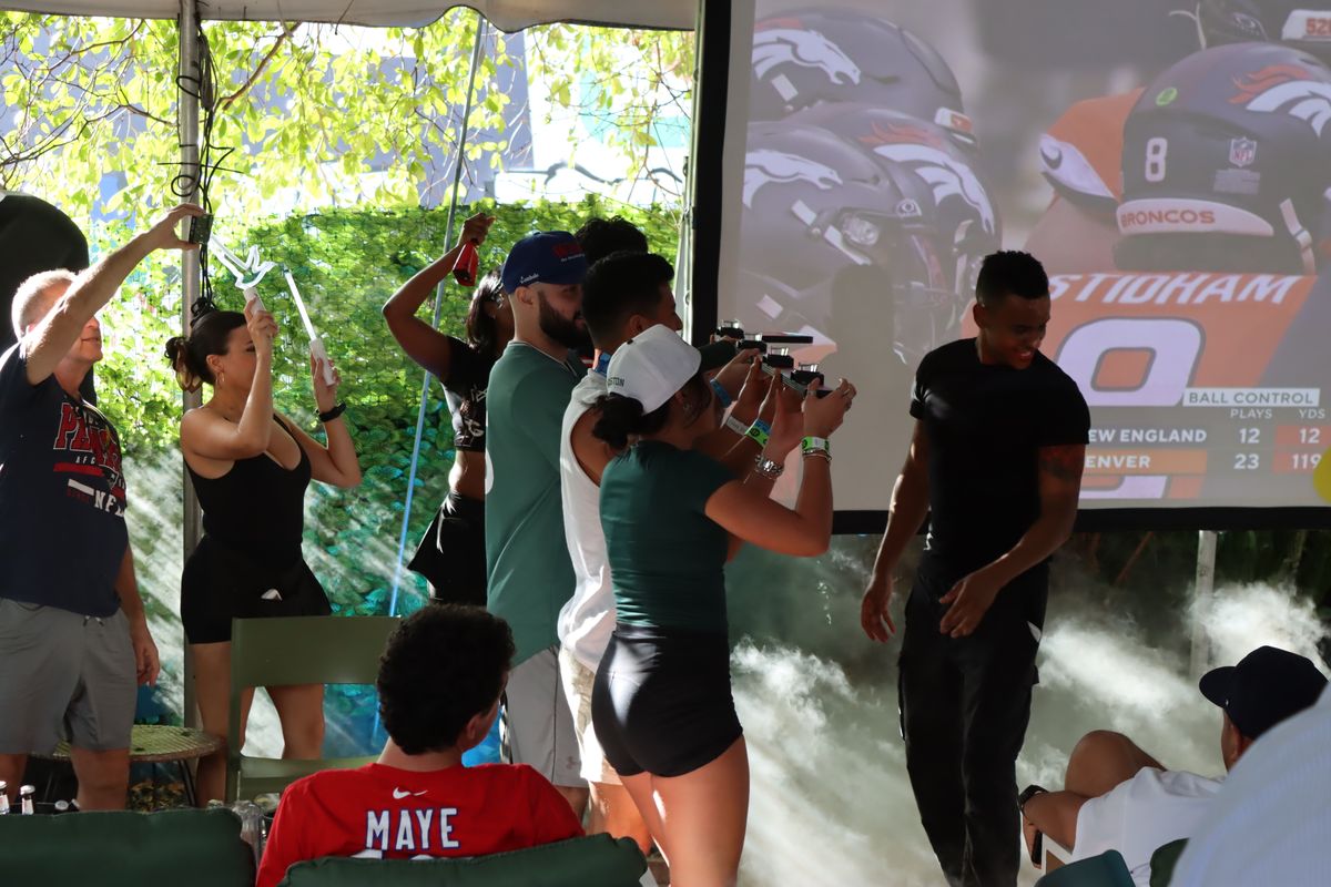 Fans on their feet in front of the giant projector screen showing an NFL game at Grails Miami, the Monday Night Football bar in Wynwood