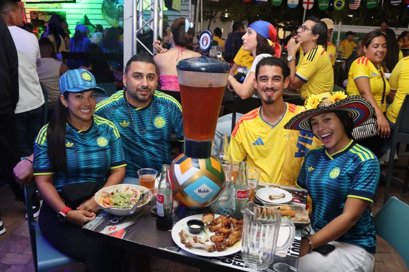 Four Colombia fans in home and away jerseys around a beer tower and shareable plates during a watch party at Grails Miami