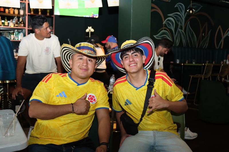 Two Colombia fans in yellow jerseys and sombreros vueltiaos giving thumbs up in the sneaker lounge at Grails Miami