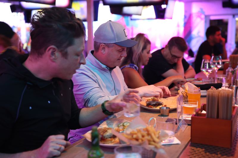 Guest in a grey trucker cap eating a burger at the Grails Miami bar counter during brunch.
