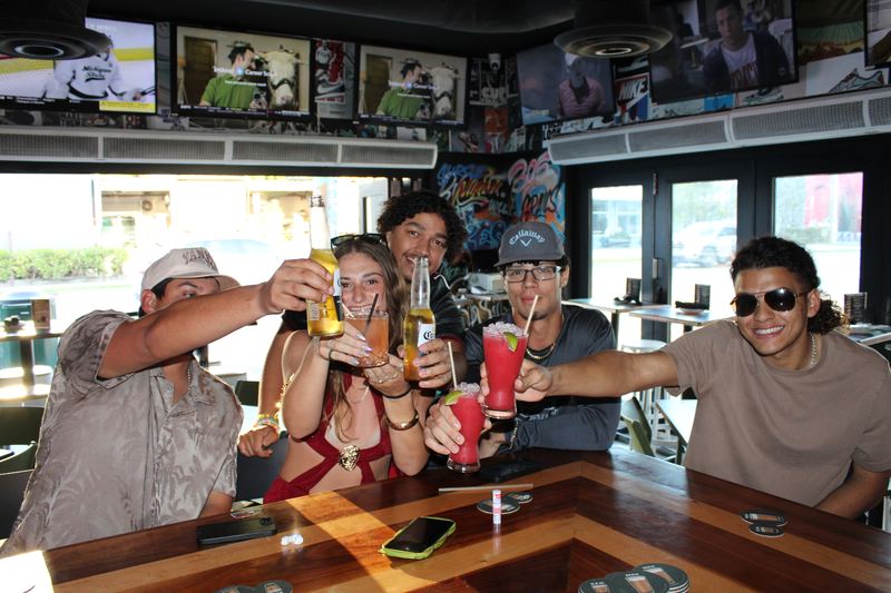 Five friends toasting beers and frozen cocktails at the Grails Miami bar counter during weekend brunch.