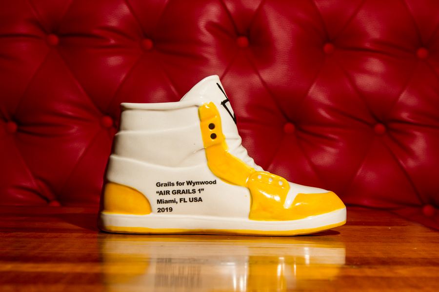 Air Grails 1 Yellow ceramic sneaker cocktail cup, white with yellow Jordan 1 panel detailing on a wooden bar at Grails Miami