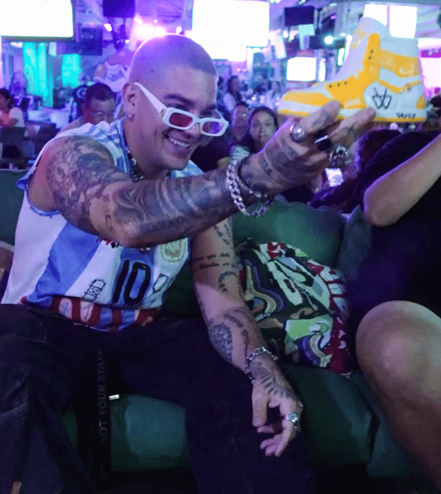 Argentina jersey fan holding up a yellow Grails sneaker cocktail at Grails Miami on World Cup night