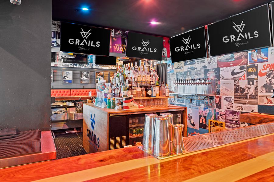 Grails Wynwood indoor bar counter with the sneaker-wall backdrop — the defining feature of the Sneaker Lounge.