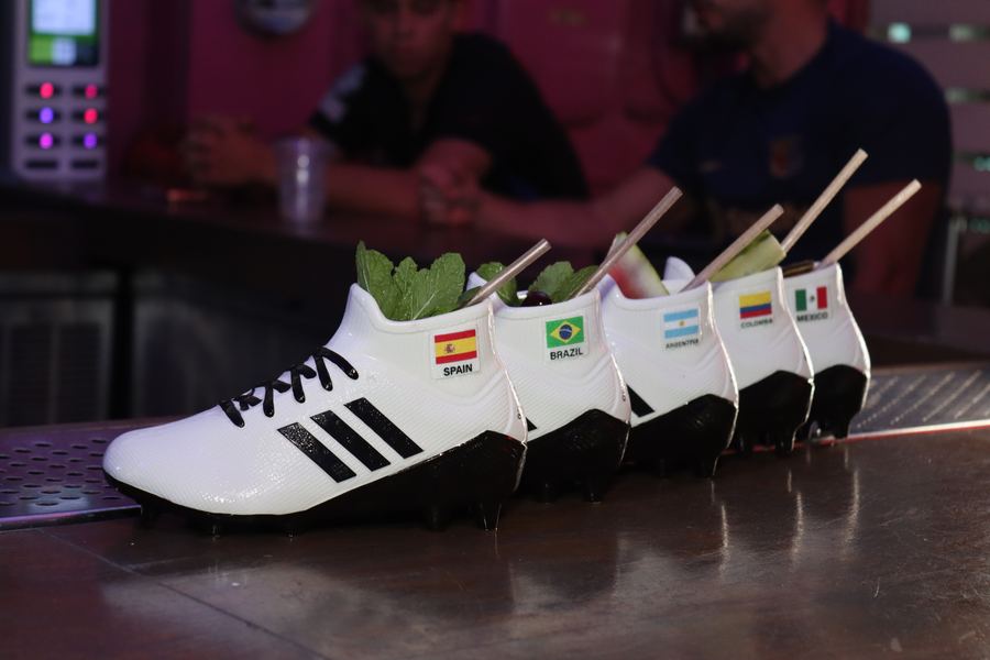 Row of five Grails Cleats ceramic World Cup cocktails on the bar at Grails Miami, Spain, Brazil, Argentina, Colombia and Mexico flag stickers visible on the heels