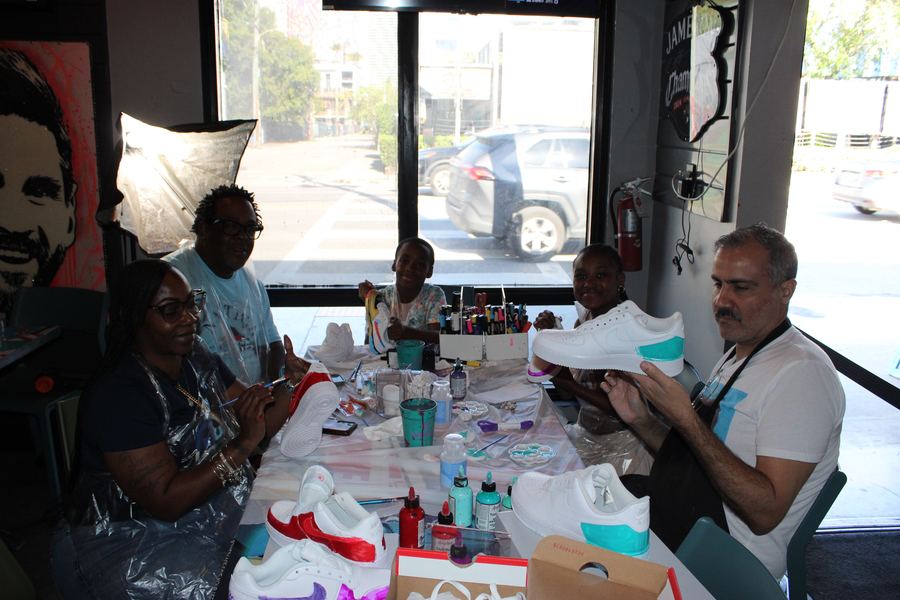 A family and instructor holding up custom-painted Nike Air Force 1 sneakers at the Kick Art Workshop
