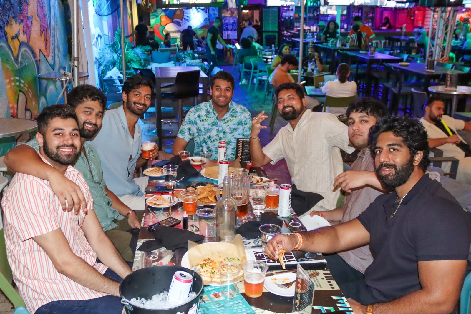 Group of seven friends smiling around a table full of food, beers, and White Claws at Grails in Wynwood.