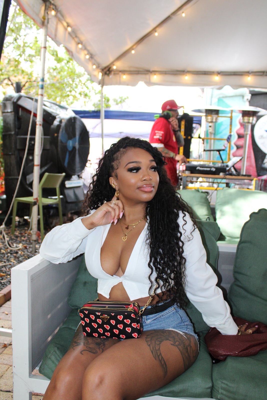 Woman in white crop top and denim shorts posing on green lounge sofa under tented patio with string lights at Grails Miami