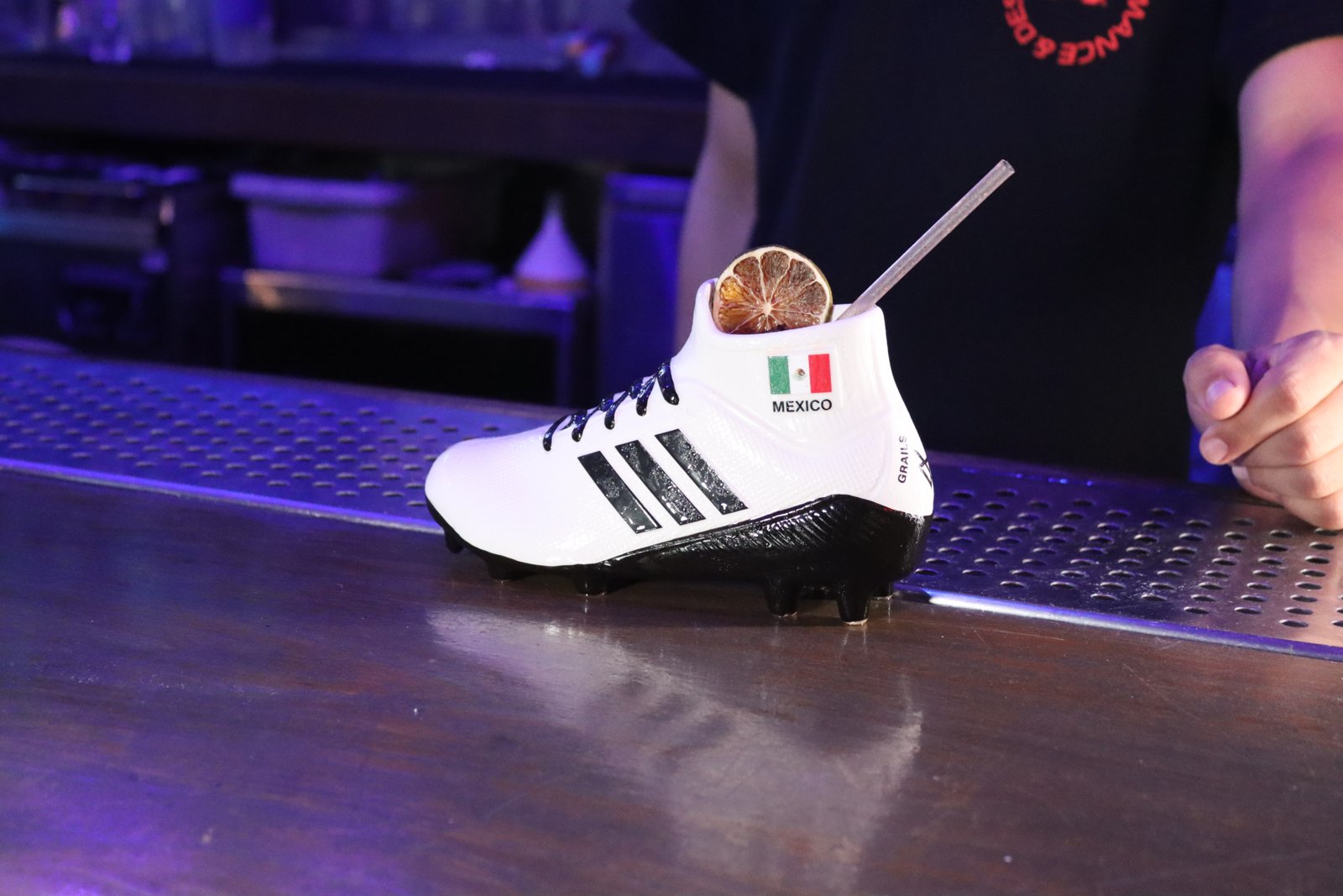Signature cocktail served in a white Adidas soccer cleat with Mexico flag, garnished with dried citrus, on the Grails bar
